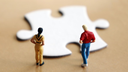 A miniature people looking down at a piece of the puzzle.