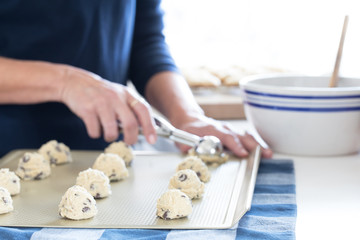 Obraz na płótnie Canvas Photograph of a woman’s hands scooping out chocolate chip cookie dough on to a cookie sheet in the kitchen 