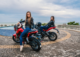 Fototapeta na wymiar Two Biker girls in leather jackets on a black and red color sport motorcycles. sea motor yachts on background