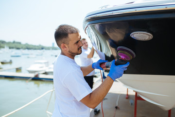 Obraz premium Boat maintenance - Man with orbital polisher polishing boat in marina. Selective focus.