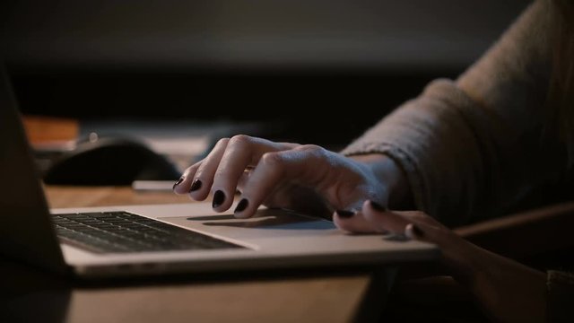 Girl using laptop trackpad and touchbar at night. Close-up. Female hands on computer touchpad. Working late at home. 4K.