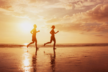 Silhouette of two runners people jogging on sunset sea beach. Healthy lifestyle background with copyspace. Family leisure activities, sport and workout. Man and woman running.