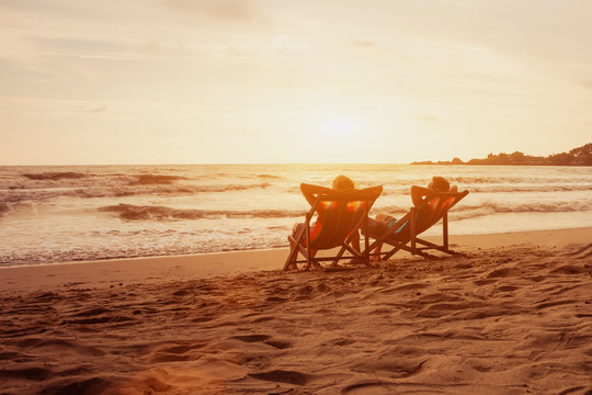 Tourism And Travel Vacation. Senior Happy Couple Relaxing In Luxurious Resort Sunset Beach In Deck Chairs. Romantic Honeymoon Holidays. Recreation Concept With Copyspace.