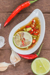 Fish sauce with slice lime and red hot chili in white bowl on wooden table, Thai food