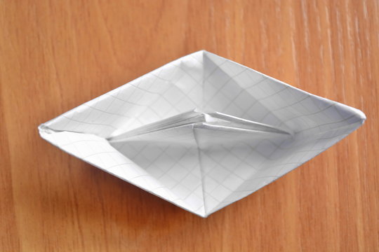Origami a paper ship from a white empty blank sheet in a cage on wooden table. Top view