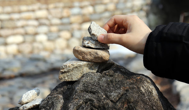 The Hands Of A Woman Laying Stones On A Stone Tower.