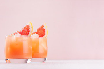 Pink cocktail with ice cubes, juice and slices grapefruit on white wood board, copy space.