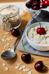 Diet and healthy Breakfast: oatmeal with cherries in a white plate on a gray tablecloth, in the background dish with cherries and a can of oatmeal