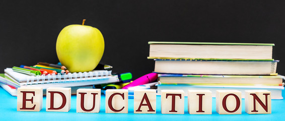 Word " Education " written by wooden cubes with school supplies on blue background against blackboard.