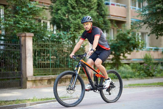 Athletic guy biker in cycling clothes and helmet looking to camera riding bicycle near beautiful buildings. Man training, improving hobby, getting ready for contest