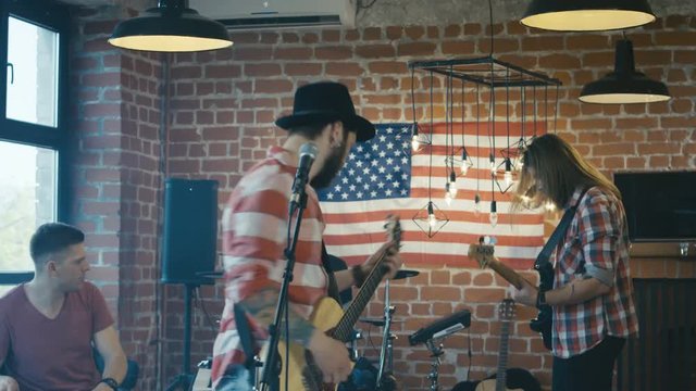 Young hipster man singing with guitar and arguing with musicians in band being discontent with playing