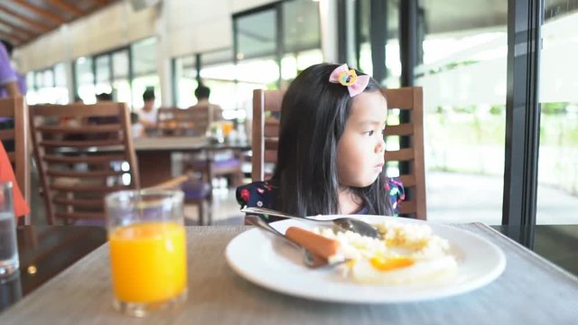 Asian children cute or kid girl student anorexia or sad with vacant on food table with fried rice, fried egg, sausage and orange juice for breakfast in restaurant before going to school for study