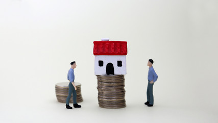A&nbsp;miniature&nbsp;house&nbsp;on&nbsp;pile&nbsp;of&nbsp;coins&nbsp;next&nbsp;to&nbsp;two&nbsp;miniature&nbsp;men.