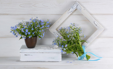 Forget-me-not flowers bouquet in clay cup, vintage casket and photo frame on white wooden shabby board
