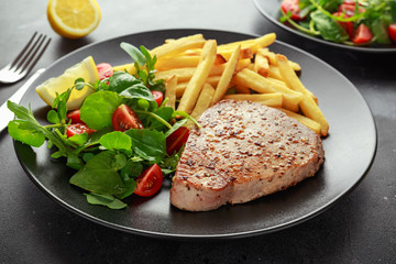 Fried Tuna Steaks on Black Plate with Fresh Green, Tomato Salad, lemon and french fries. healthy sea food