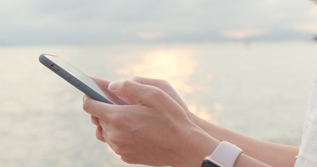 Hand holding cellphone with the sunset sea background