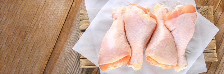 Raw chicken legs on a cutting board on an old wooden table.