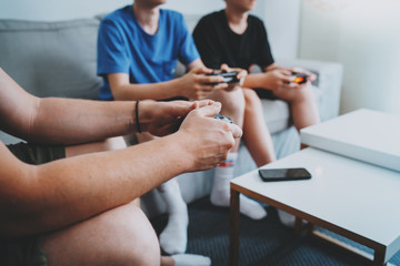 Young teenage sitting on a sofa in living room and playing video games. Family relaxing time at home concept. Closeup.