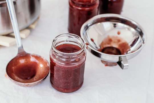 Preparing marmalade at home. Fresh red fruits from own garden or farmer market. Self supply, traditional canning with boiling in sugar. Filling glass jars with hot jam.