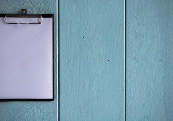 Clipboard with white sheet on wood background. Top view.Vintage style.