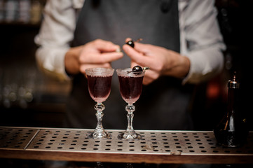 Barman decorating two glasses filled with strong summer Arnaud cocktail