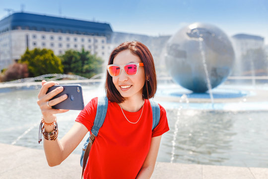 Happy tourist woman doing selfie and photographing palace residence of President and fountain with globe. Travel in Bratislava and Slovakia concept