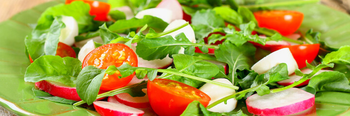 Vegetarian salad of arugula, tomato, radish and mozzarella cheese on an old wooden table.