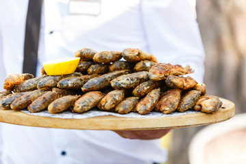 Dish of whole fish on a tray in the hand of the waiter. Male waiter handing a dish, and holding a tray with baked fish and garnish, close-up