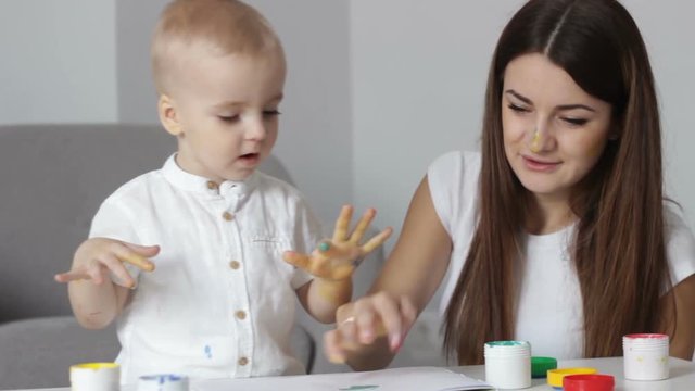 Nanny, childminder teaches little boy preschooler painting by hands and fingers