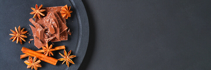 Pieces of chocolate, cinnamon and star anise on a dark grey table.