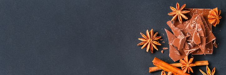 Pieces of chocolate, cinnamon and star anise on a dark grey table.