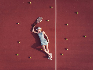 Overhead top view of young Caucasian teen model wearing fashionable tennis dress, lying on tennis...