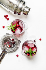 Cranberry cocktail with ice, rosemary and berries, bar tools, white background, top view