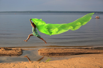 Młoda dziewczynka skacze przez wodę z długą zieloną chustą.
