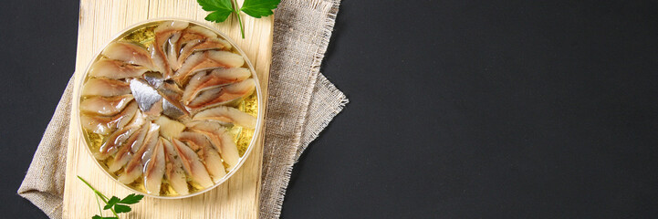 Marinated herring in oil on a wooden board on a gray dark table. Snack. Top view. Copy space.