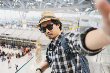 Asian man tourist taking a selfie with smart phone camera in airport.