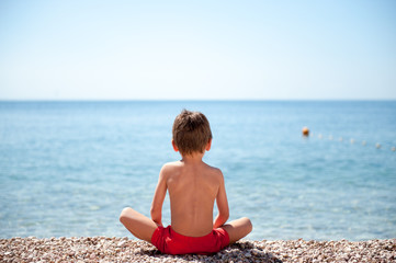 Fototapeta na wymiar healthy little child sitting on sea shore beach watching at horizon meditation