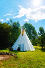 white teepee indian tent standing in beautiful summer landscape.