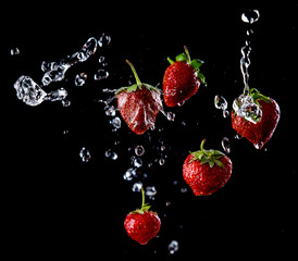 fresh strawberries fall in a spray of water, bright red berries