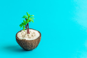 Coconut half with sand and palm tree isolated on turquoise background abstract concept.
