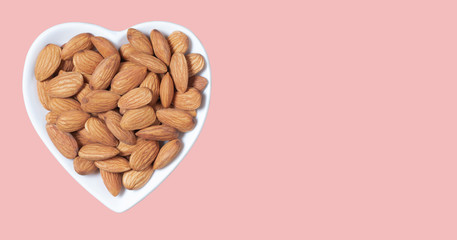 Almond seedlings in a white heart-shaped cup are placed on pink background