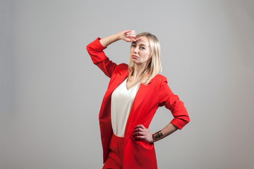 Young beautiful white blond girl in a bright red strict suit with a jacket and white blouse standing in a pose on a white isolated background