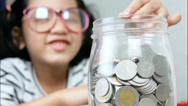 Asian little girl putting the coin in to a glass jar shallow depth of field select focus on jar