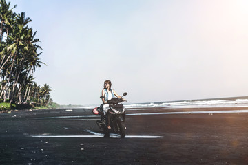 Young woman driving a scooter at the beach with black sand. Bali island.