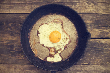 One fried egg in a frying pan on a wooden background in rustic style close-up