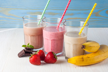 Glasses of milkshakes with chocolate, strawberry, banana flavor, with ice cream on wooden blue and white background. Sweet drinks for summer concept. Shakes and smoothies. Milk shake and cocktail.
