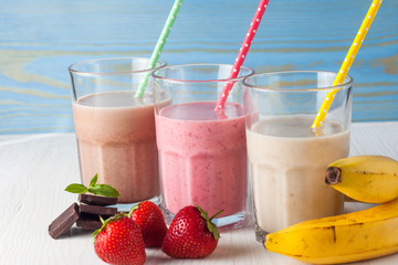 Glasses of milkshakes with chocolate, strawberry, banana flavor, with ice cream on wooden blue and white background. Sweet drinks for summer concept. Shakes and smoothies. Milk shake and cocktail.
