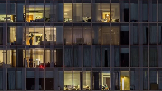 Windows of the multi-storey building of glass and steel lighting inside and moving people within timelapse