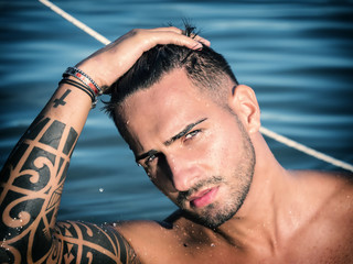 Attractive young shirtless athletic man standing in water in sea or lake, wearing shorts, looking...