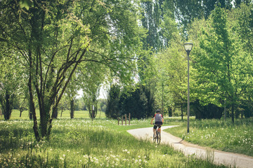 Fototapeta premium back view of man cycling in a park. Green nature with meadow in flower and trees 